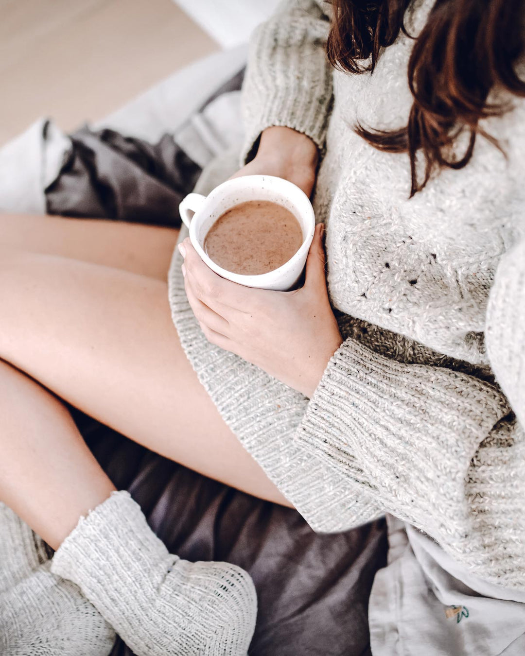 Hot cup of hot chocolate on a cozy couch surrounded by knits, jumpers and socks
