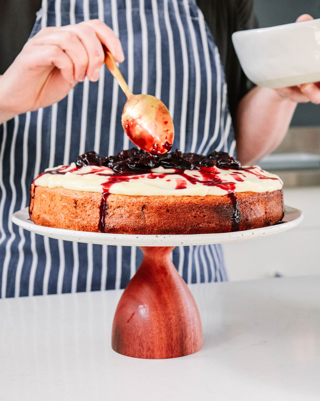 Lise Walsh decorating her tea cake with vanilla cream icing and cherry syrup on her Winterwares handmade cake stand