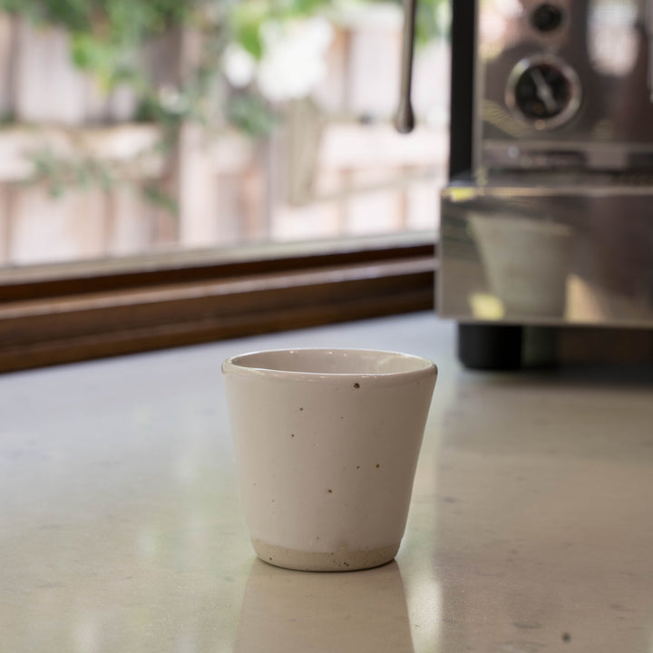 White ceramic cup on a countertop with an espresso machine in the background